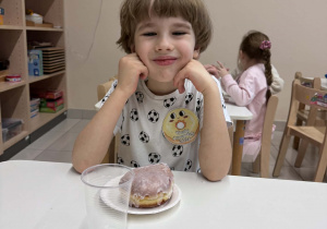 uśmiechniety chłopiec siedzi przy stoliki z pączkiem