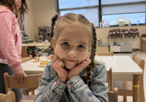 uśmiechnieta dziewczynka siedzi przy stoliki z pączkiem