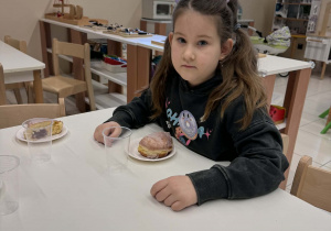 dziewczynka siedzi przy stoliku z pączkiem