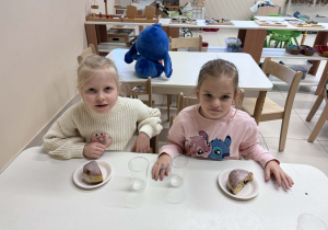 dwie dziewczynki siedzą przy stoliku z pączkami