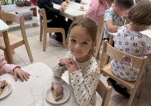uśmiechnieta dziewczynka siedzi przy stoliku z pączkiem