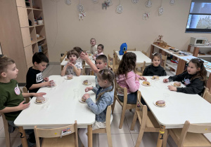 dzieci siedzą przy stolikach z pączkami do zjędzenia