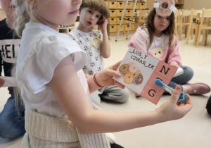 dziewczynka trzyma obrazek z brakującymi literkami i trzyma klamerkę na literce, której brakuje