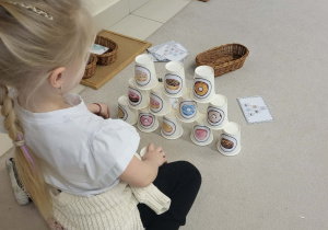 dziewczynka według wzoru układa wieże z kubeczków, na których są pączki