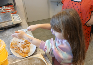 Dziewczynka posypuje cukrem pudrem pączki