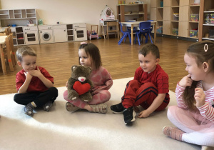 dzieci siedzą w kole i podają misia