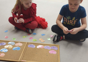 chłopiec z dziewczynką składają połówki serc w całość łącząc sylaby i czytają wyraz