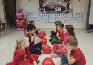 przedszkolaki siedzą na dywanie i pomiędzy nimi jest balon