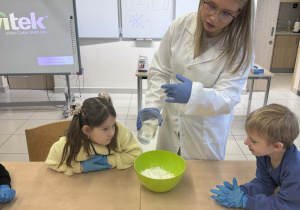 chłopiec i dziewczynka obswerują eksperyment,który wykonuje uczenica