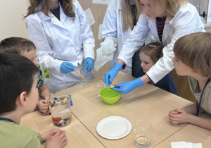 dzieci obserwują eksperyment wykonuwany przez panią od chemi i uczenice