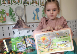 dziewczynka prezentuje książkę na temat wyginięcia dinozaurów