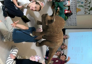 dzieci siedzą na dywanie z dinozaurem , który jest w środku