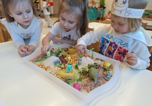 dzieci bawia sie dinozaurami na tacy sensorycznej