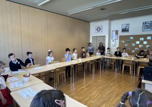 dzieci siedzą przy stoliku i słuchają