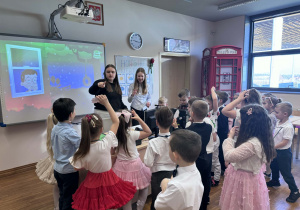 dzieci stoją przed uczenicami i wykonują zadanie z angielskimi podpisami