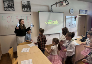 uczenica trzyma obrazki z pogoda i dzieci do niej podchodzą wykonując zadania "find a"-"znajdz"