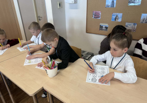 dzieci siedzą przy stoliku i kolorują obrazki z pogodą