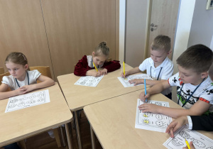 dzieci siedzą przy stoliku i kolorują obrazki z pogodą