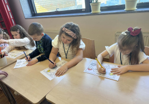 dzieci siedzą przy stoliku i kolorują obrazki z pogodą