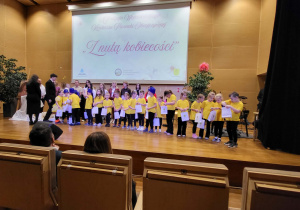 dzieci stoją na scenie i trzymają torebki z upominkami na występ