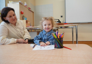 dziewczynka siedzi przy stoliku i koloruje malowankę