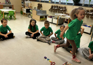 dzieci siedzą w kole jedna dziewczyna idzie w sronę swojego miejsca