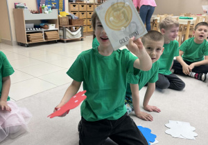 chłopiec siedzi w kole i pokazuje wylosowany obrazek ze złotą monetą