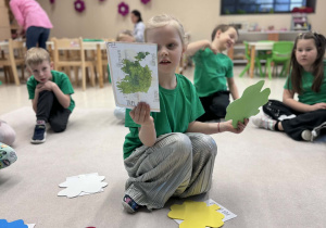 dziewczynka siedzi w kole i pokazuje wylosowany obrazek z mapą Irlandii