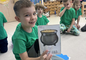 chłopiec siedzi w kole i pokazuje wylosowany obrazek z garnkiem złota
