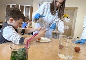 chłopiec wykonuję eksperyment z butelką i jajkiem, obok niego stoi uczenica liceum