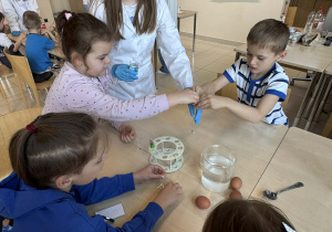 dzieci wsypują do menzurki, którą trzyma uczenica,skorupki jajek