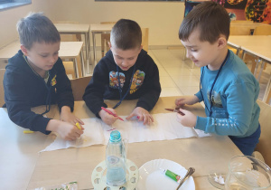 trzej chłopcy malują mazakami kawałek ręcznika papierowego