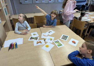 na stoliku leżą porozrzucane obrazki a dzieci siedzą i patrzą w lewą stronę