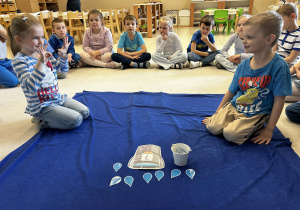 Chłopiec liczy pace pokazywane przez dziewczynkę i dopasuje odpowiednia cyfrę na wiaderku i ilość kropelek