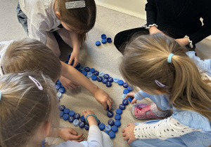 Dzieci pracują w grupie tworząc figury geometryczne z niebieskich zakrętek