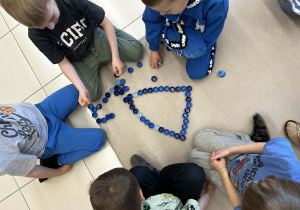 Dzieci pracują w grupie tworząc figury geometryczne z niebieskich zakrętek