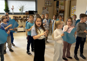 Dzieci stukają w niebieskie kartki w rytm muzyki