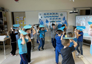 Dzieci chodzą z niebieską kartką nad głową tworząc parasol