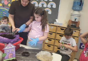 pani Ewa pomaga dziewczynce nabrać ziemie na łopatkę