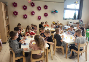 Dzieci siedzą przy stolikach i jedzą czekoladowe babeczki