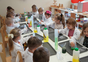 dzieci siedzą przy stoliku w białych fartuszkach