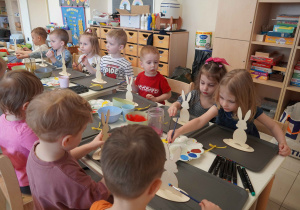 Trzylatki siedzą przy stoliku z drewnianymi zającami