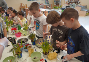 Sześciolatki nasypują ziemię i piasek do naczynia