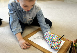 Chłopiec próbuje kolorować obrazek w rękawicy kuchennej