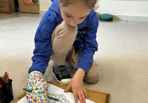 Chłopiec próbuje kolorować obrazek w rękawicy kuchennej