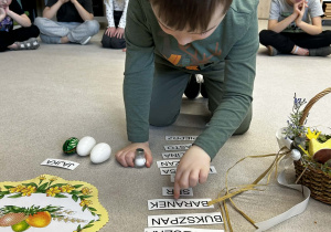 Chłopiec dopasowuje podpisy do symboli wielkanocnych na dywanie.