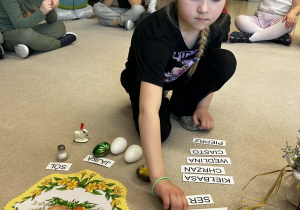 Dziewczynka dopasowuje napis do przedmiotu z koszyczka wielkanocnego.