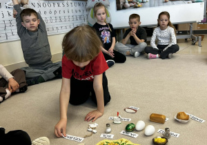 Chłopiec przyporządkowuje nazwy produktów do ich odpowiedników na dywanie.