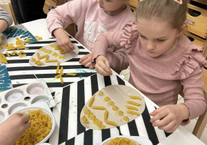 Dziewczynki precyzyjnie przyklejają suchy makaron do szablonów jajek.