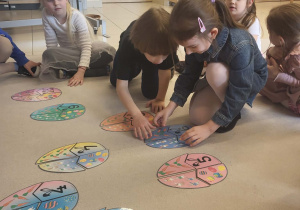 Dzieci wspólnie układają wielkanocne puzzle matematyczne na dywanie.